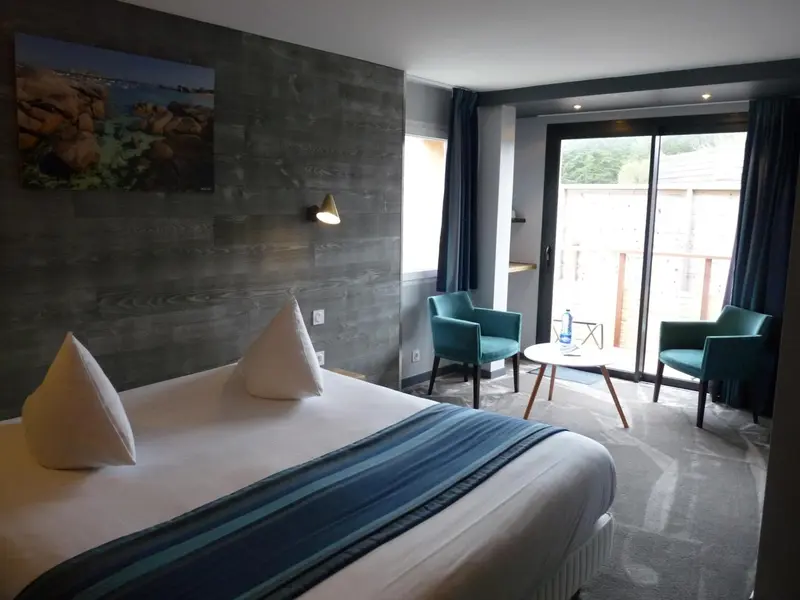 Une chambre lumineuse avec un lit fait et un coin salon près d'une baie vitrée.