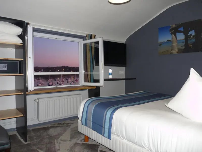 Une chambre avec un lit simple et une vue sur un port au crépuscule.