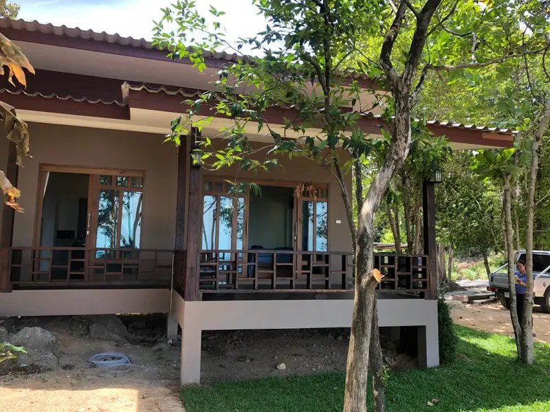 Façade d'un bungalow sur pilotis avec une terrasse ombragée.