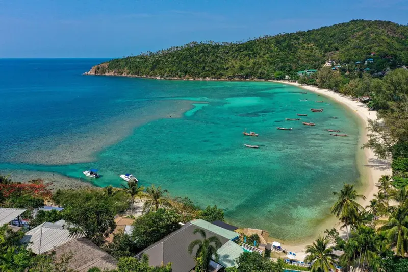 Vue aérienne d'une plage de sable blanc bordée d'une eau turquoise et d'une végétation luxuriante.