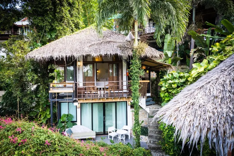 Petites maisons sur pilotis avec terrasses fleuries dans un jardin tropical.
