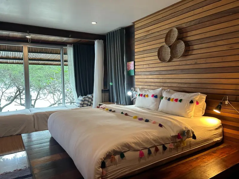 Une chambre lumineuse avec un grand lit décoré de coussins colorés et une vue sur l'extérieur.