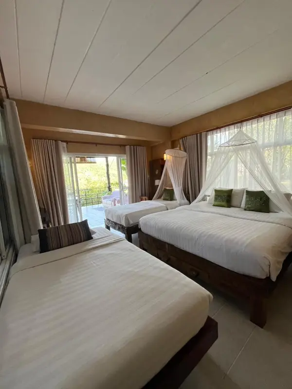 Chambre avec deux lits jumeaux et moustiquaire, donnant sur une terrasse.