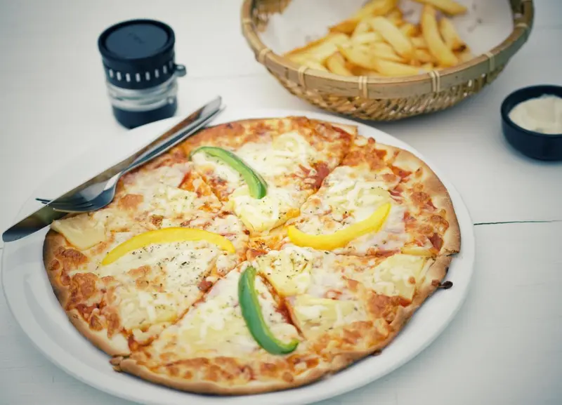 Une pizza garnie de légumes et de fromage est servie sur une table blanche.
