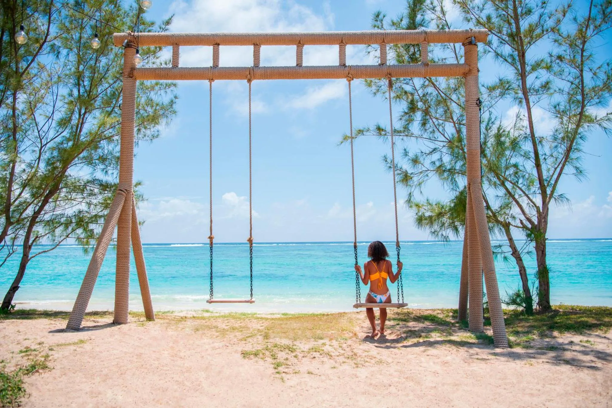 Une personne assise sur une balançoire en bois face à la mer turquoise.