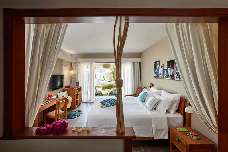 Chambre lumineuse avec un grand lit et vue sur une plage.