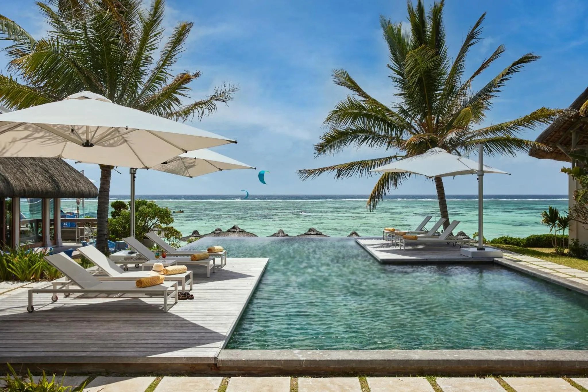 Transats blancs disposés autour d'une piscine à débordement avec vue sur la mer.
