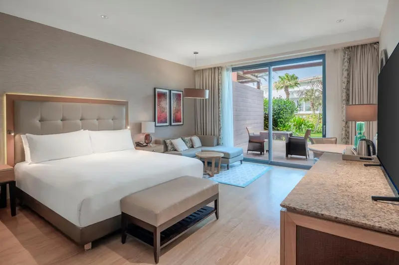 Une chambre lumineuse avec un grand lit et un espace salon donnant sur une terrasse.
