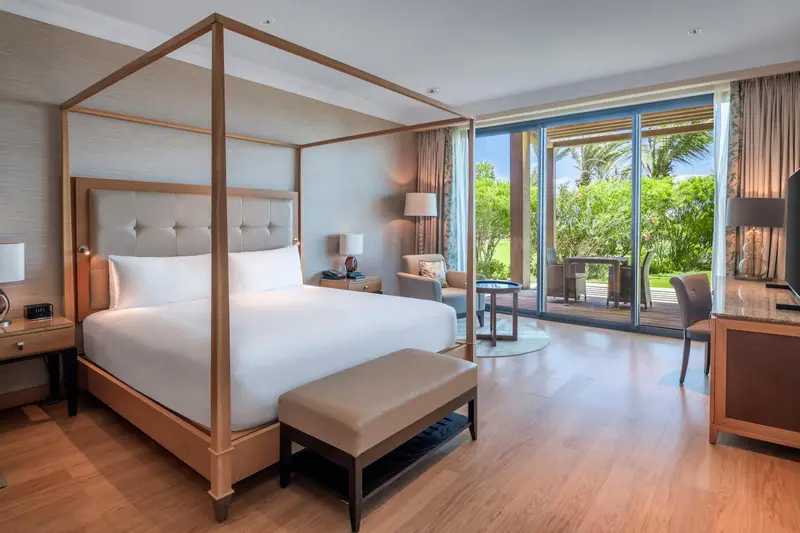 Une chambre lumineuse avec un grand lit à baldaquin et vue sur une végétation luxuriante.
