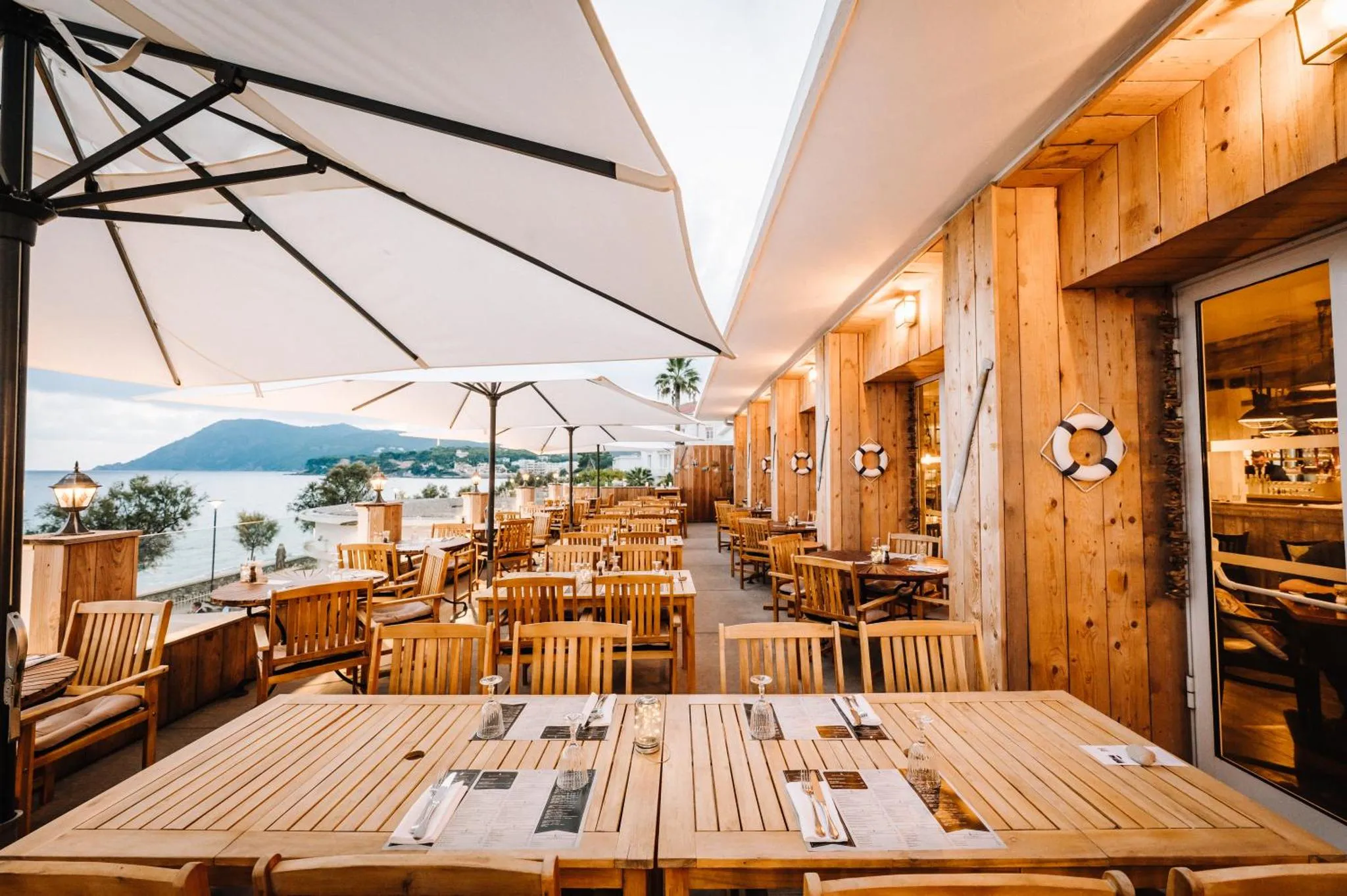 Une terrasse ombragée avec des tables et des chaises en bois donnant sur la mer.