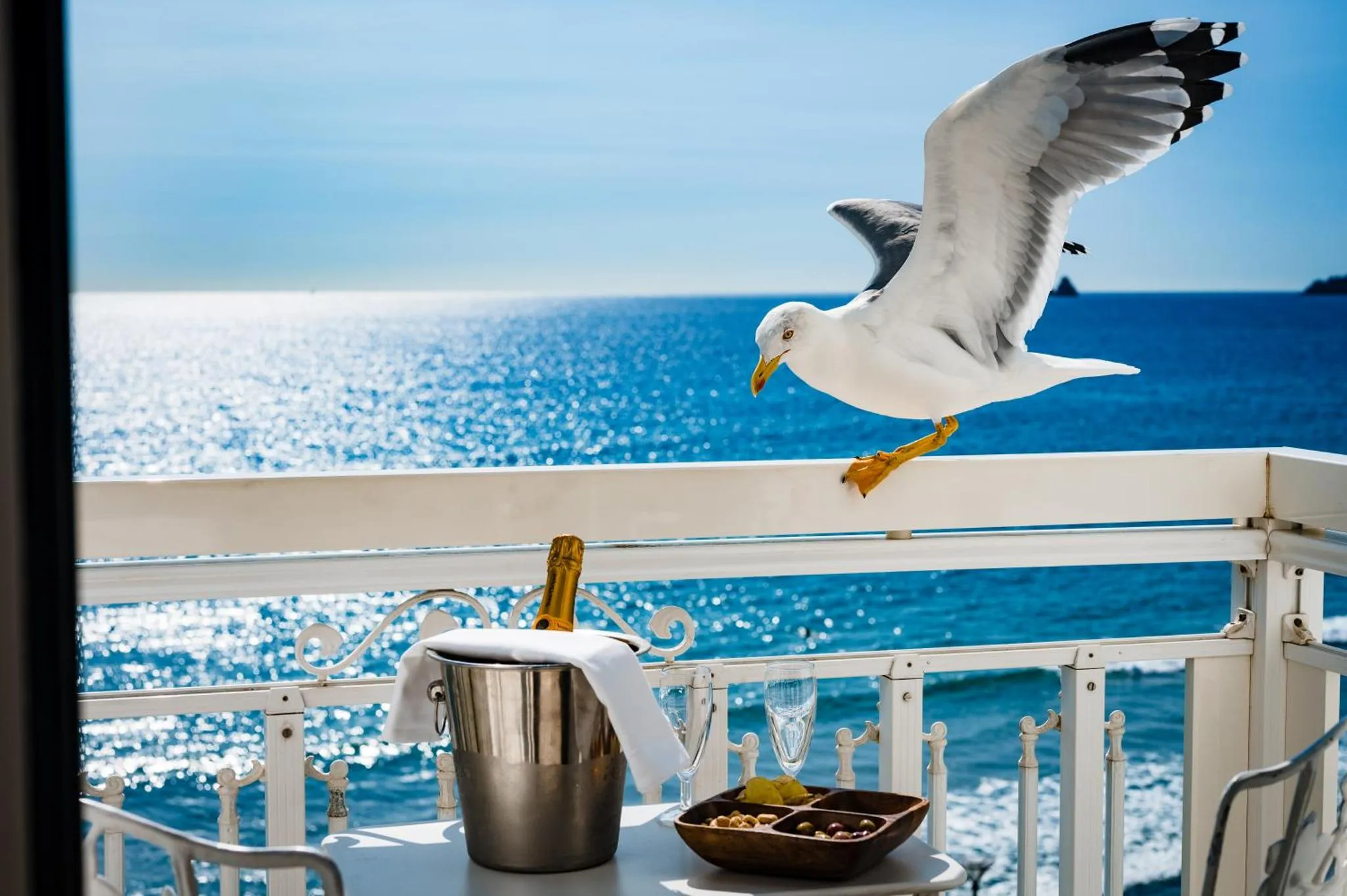 Une vue sur la mer depuis un balcon avec une bouteille de champagne et des verres.