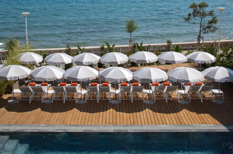 Terrasse en bois avec transats et parasols blancs au bord de l'eau.