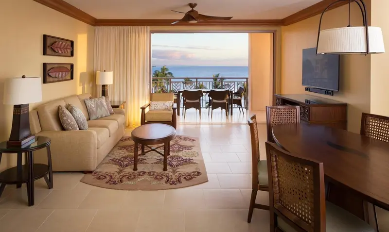 Un salon lumineux s'ouvre sur une terrasse avec vue sur la mer au coucher du soleil.
