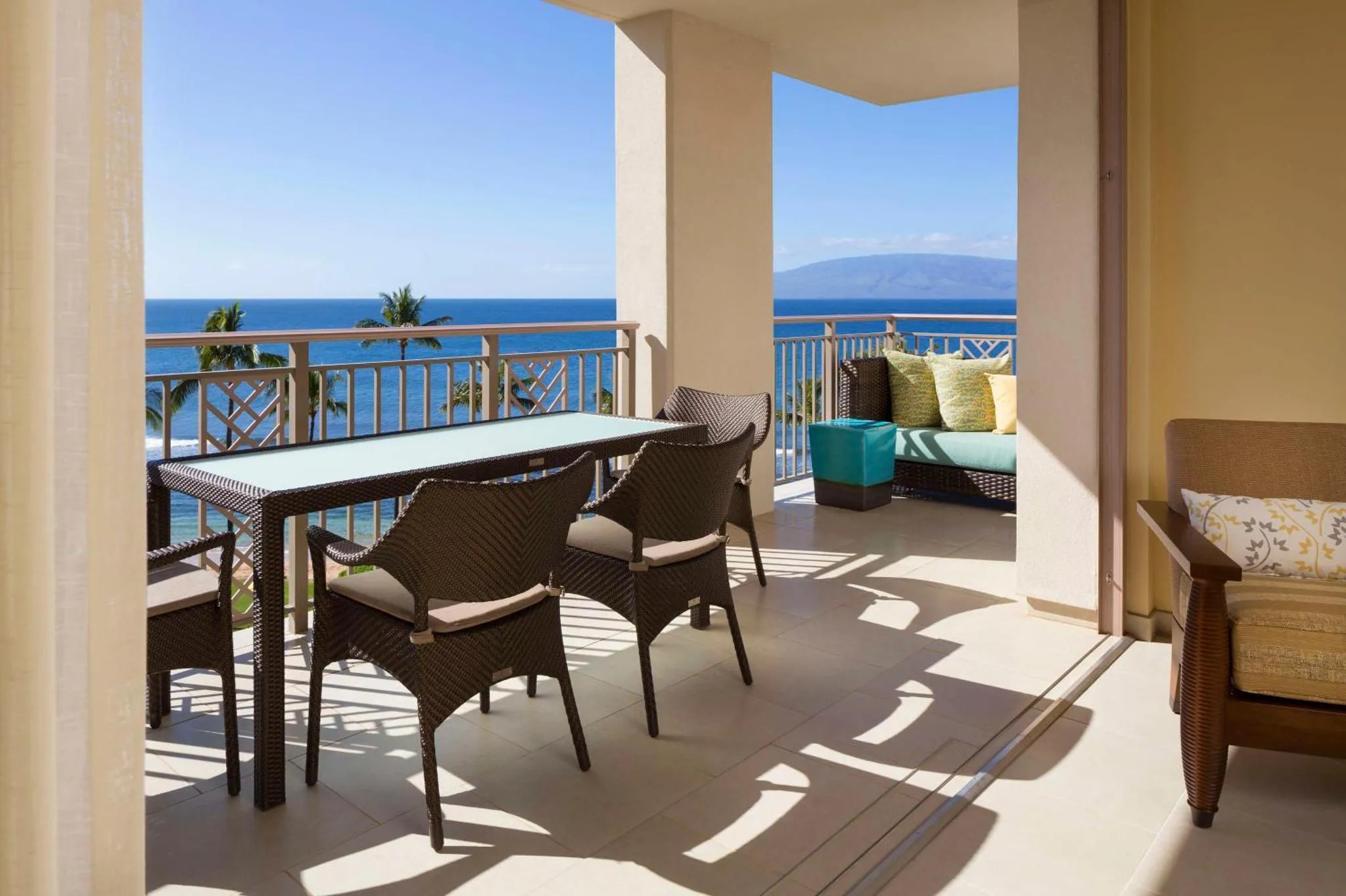 Une table à manger en osier sur une terrasse avec vue sur la mer.
