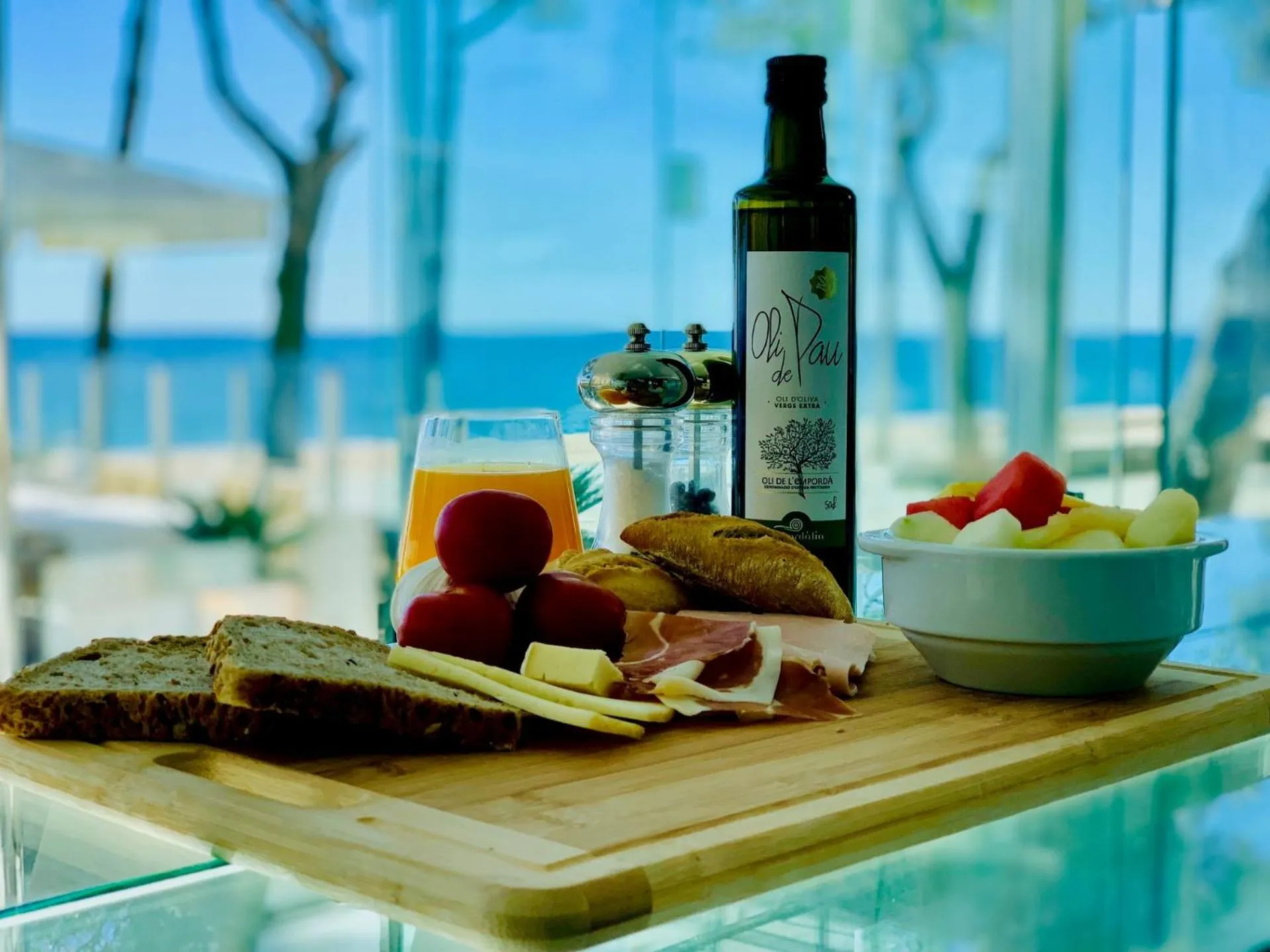 Une table en bois présente un petit-déjeuner avec des fruits, du pain, du fromage et une bouteille d'huile d'olive.