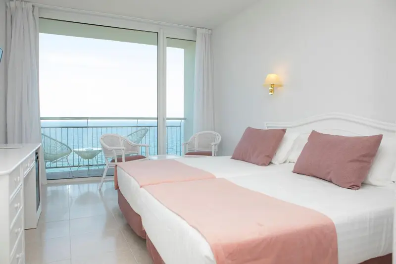 Une chambre lumineuse avec un grand balcon donnant sur la mer.