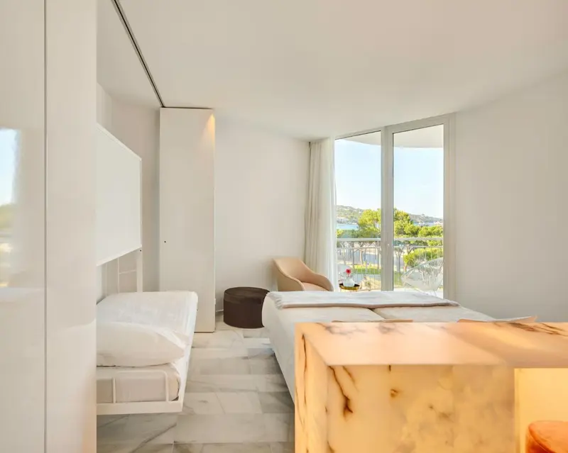 Chambre lumineuse avec un lit et un coin salon donnant sur une vue mer.