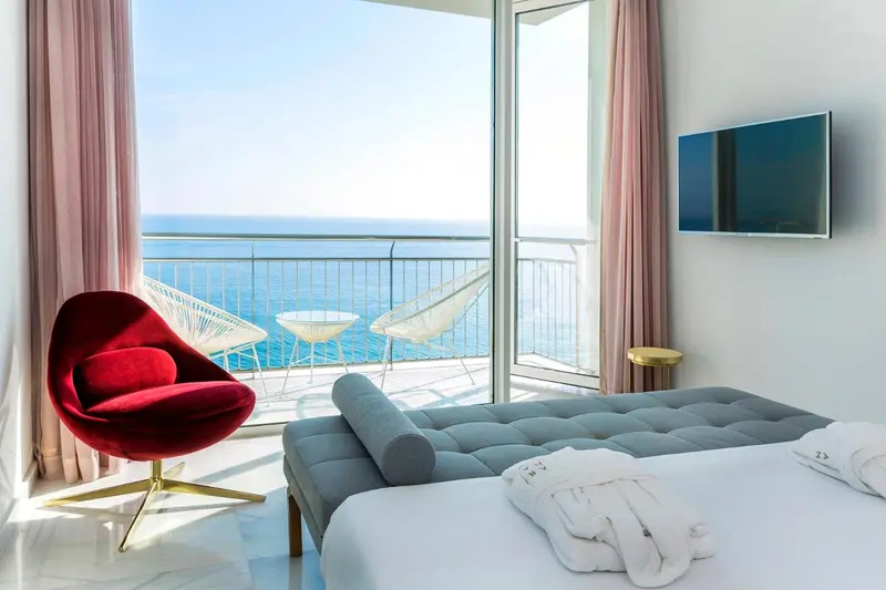Une chambre lumineuse s'ouvre sur une terrasse avec vue sur la mer.