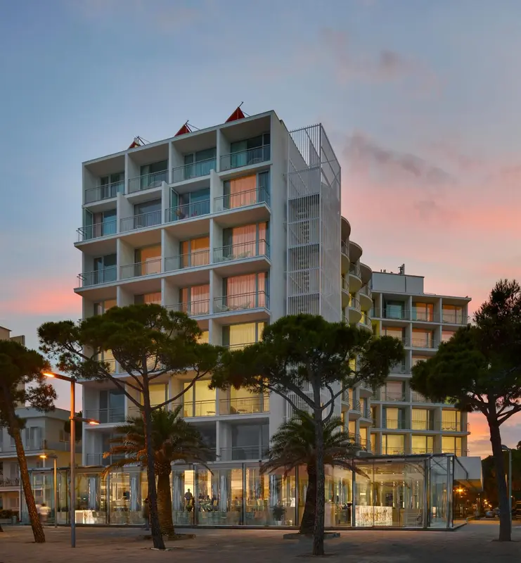 Bâtiment moderne avec des balcons et des arbres au premier plan, illuminé par le ciel crépusculaire.