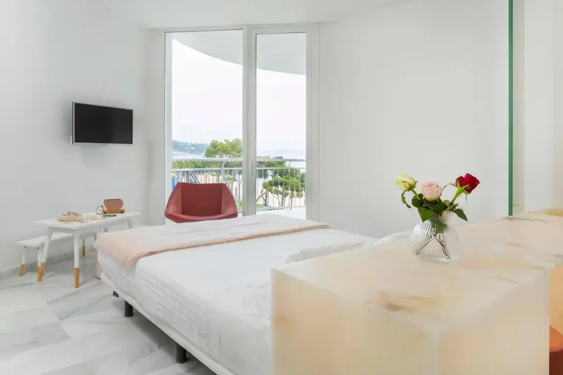 Une chambre lumineuse avec un lit fait et une vue sur la mer.