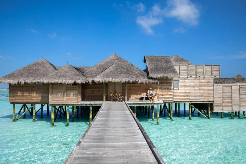 Maisons sur pilotis en bois avec toits de chaume au-dessus d'une eau turquoise.