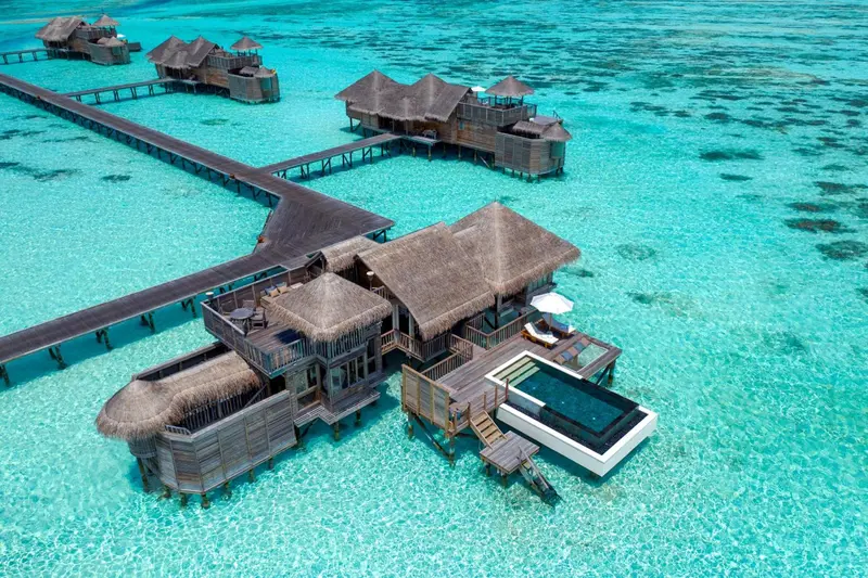 Vue aérienne de bungalows sur pilotis au-dessus d'une eau turquoise.