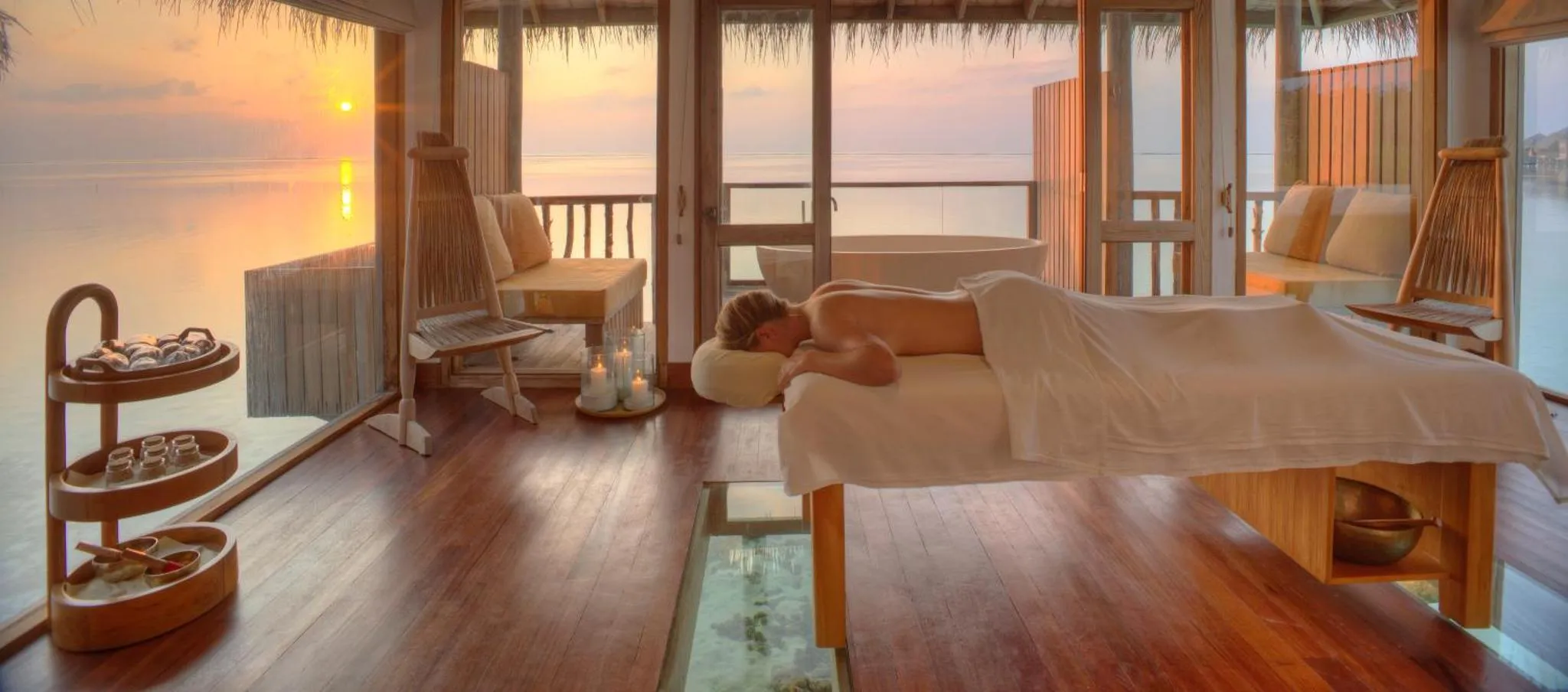 Une personne reçoit un massage sur une terrasse en bois avec vue sur la mer.