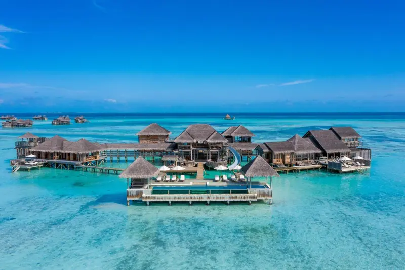Vue aérienne d'un complexe hôtelier sur pilotis au milieu d'un lagon turquoise.