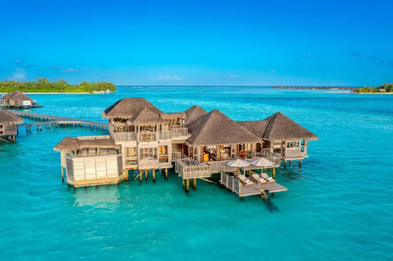 Vues aériennes de bungalows sur pilotis au-dessus d'une eau turquoise.
