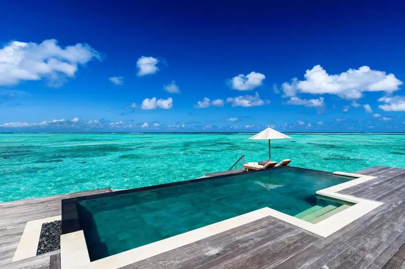 Une piscine à débordement turquoise offre une vue sur l'océan clair et le ciel bleu.