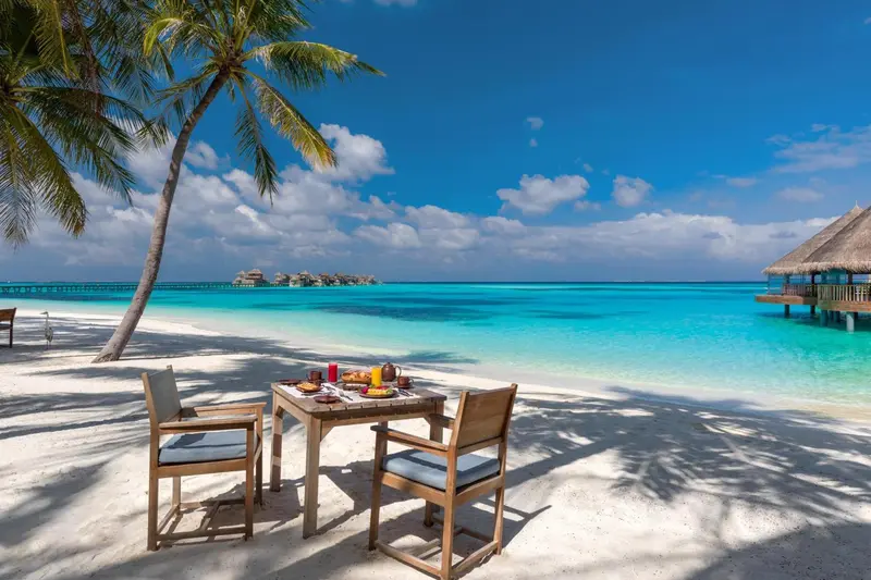 Table de petit-déjeuner dressée sur une plage de sable blanc face à une mer turquoise.