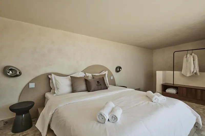 Une chambre lumineuse avec un grand lit recouvert de coussins blancs et gris.