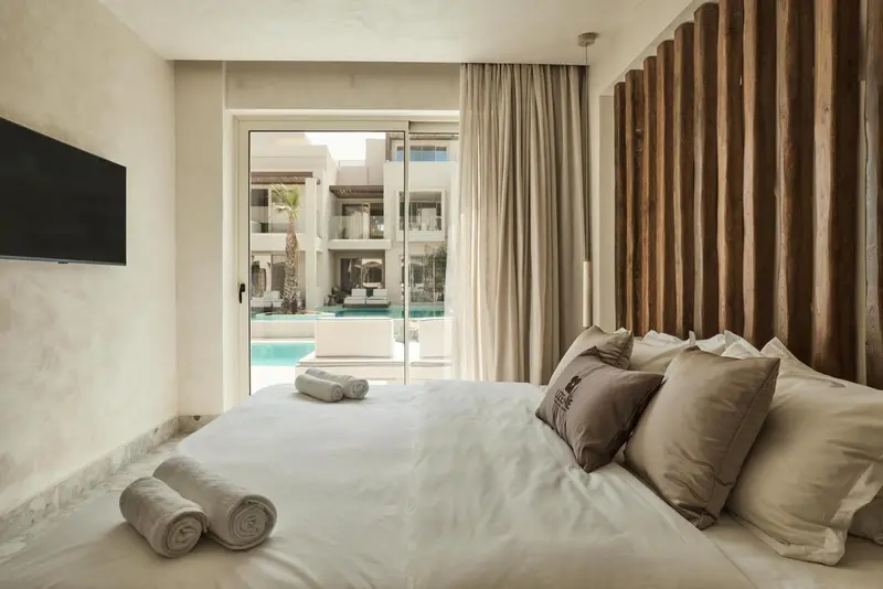 Une chambre lumineuse avec un grand lit et un accès à une piscine.