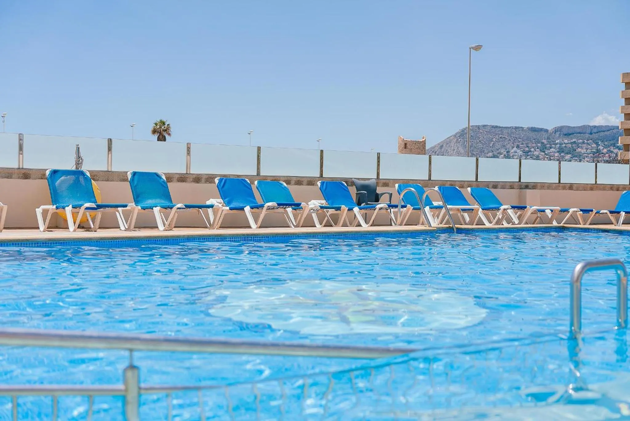 Transats bleus alignés au bord d'une piscine ensoleillée.