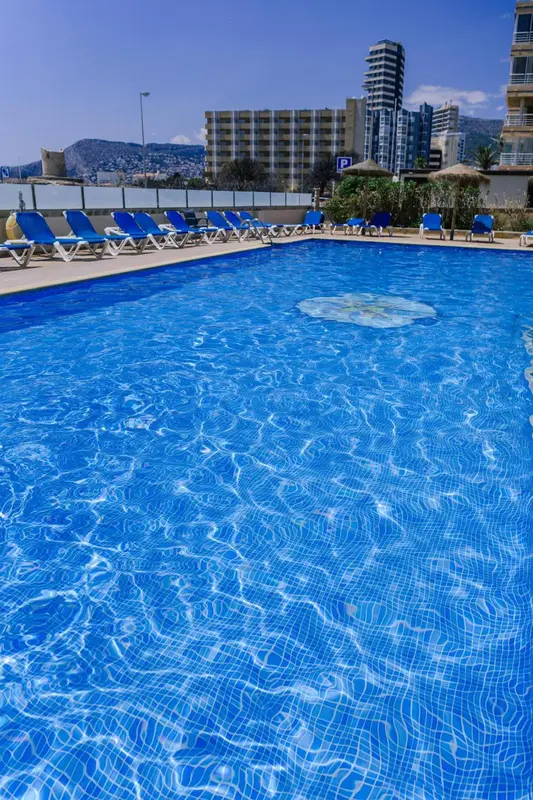 Transats bleus alignés au bord d'une piscine turquoise sous un ciel bleu.