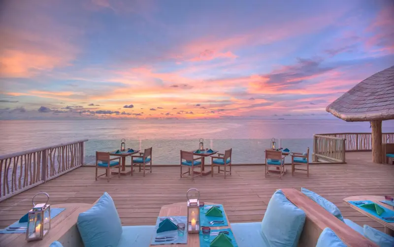 Tables de restaurant en terrasse avec vue sur la mer au coucher du soleil.