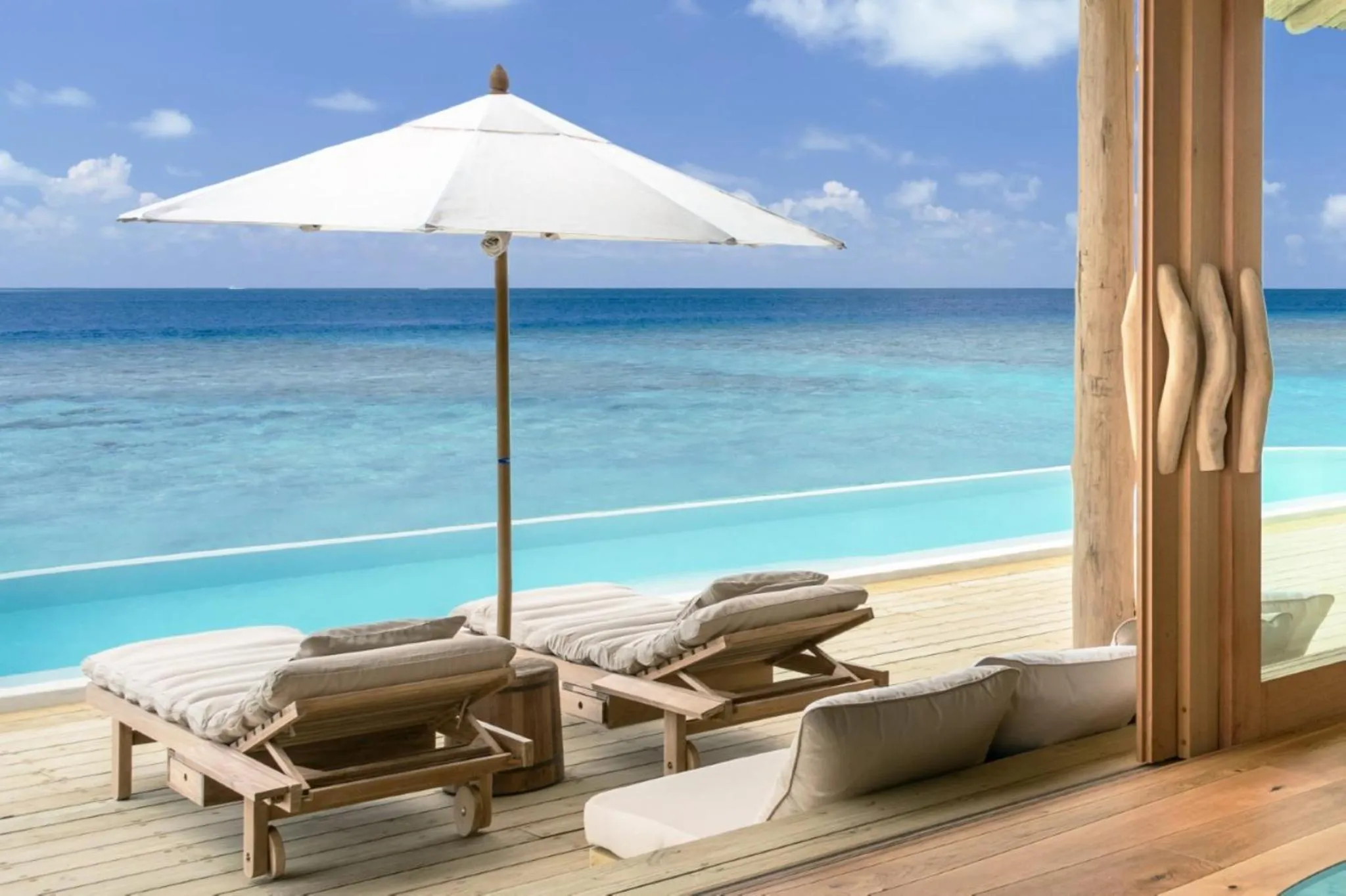Transats en bois sur une terrasse avec vue sur la mer turquoise.