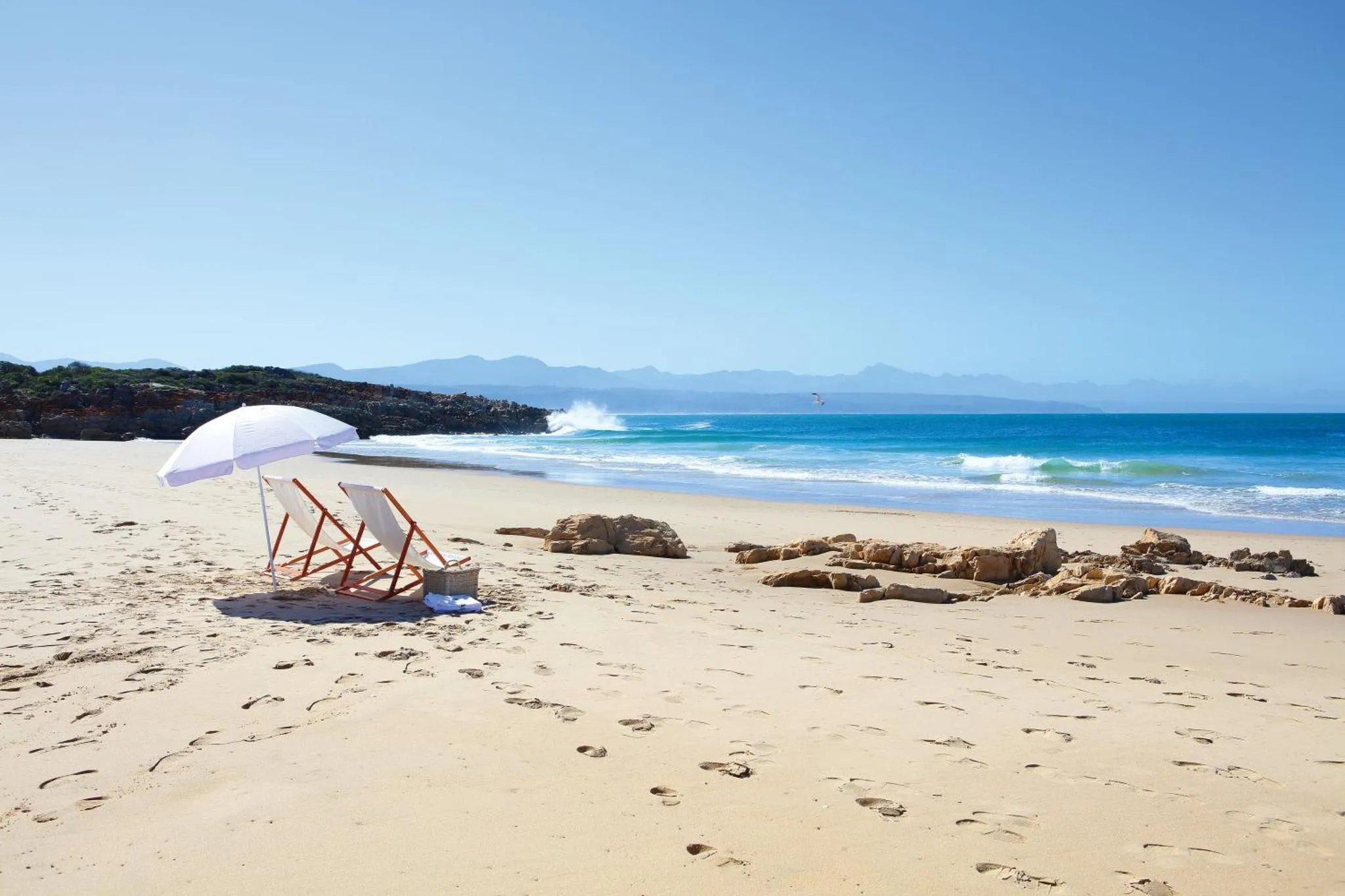 Deux transats et un parasol sur une plage de sable fin face à la mer.