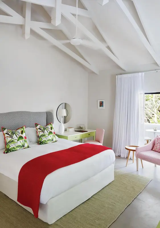 Une chambre lumineuse avec un lit recouvert d'une couverture rouge et des coussins colorés.