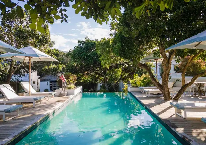 Une piscine rectangulaire bordée d'une terrasse en bois et de transats sous des parasols.