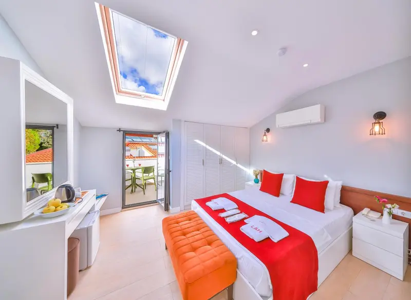 Chambre lumineuse avec un lit recouvert d'une courtepointe rouge et un accès à une terrasse.