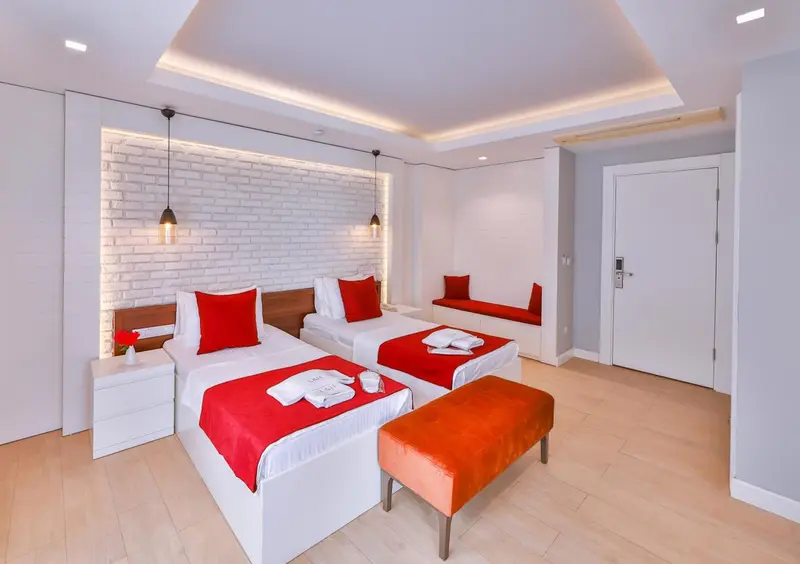 Chambre lumineuse avec deux lits et une banquette rouge.