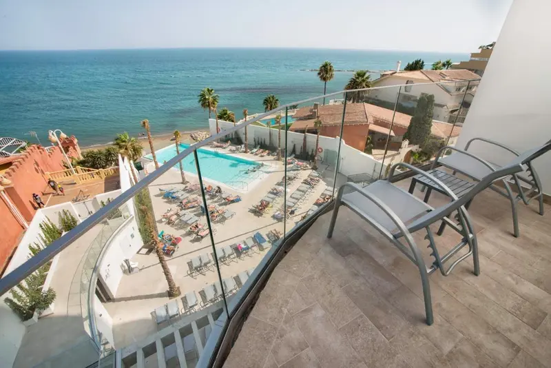Vue d'une terrasse avec transats donnant sur une piscine et la mer.