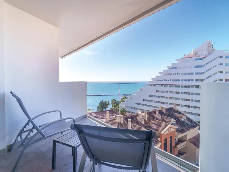 Vue d'une terrasse avec transats donnant sur la mer et des bâtiments.