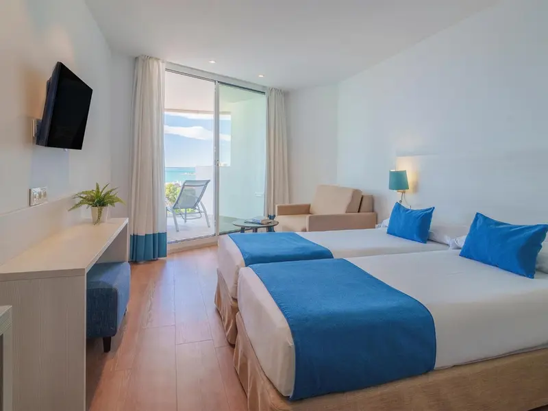 Chambre lumineuse avec deux lits et un canapé face à une baie vitrée.
