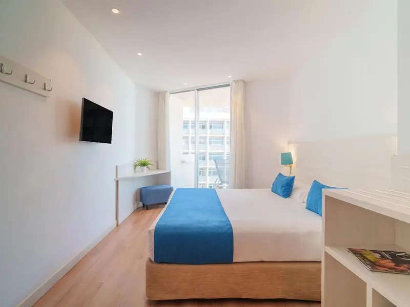 Chambre lumineuse avec un lit bleu et une vue sur l'extérieur.
