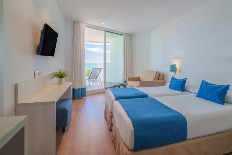 Chambre lumineuse avec deux lits et balcon donnant sur la mer.