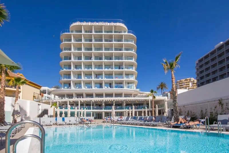 Bâtiment blanc moderne avec des transats bleus autour d'une piscine turquoise.
