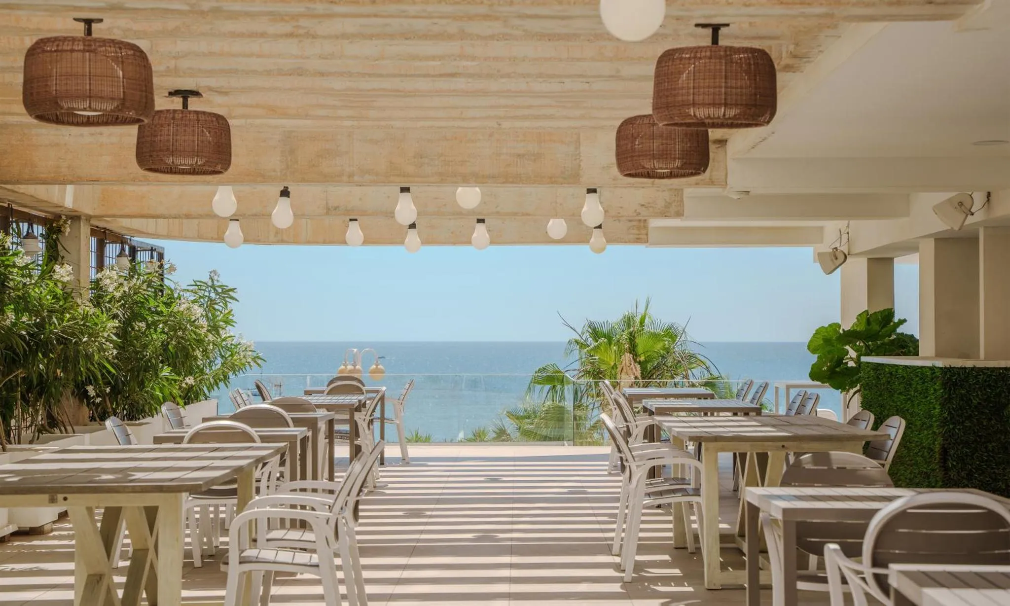 Terrasse ombragée avec tables et chaises donnant sur la mer.