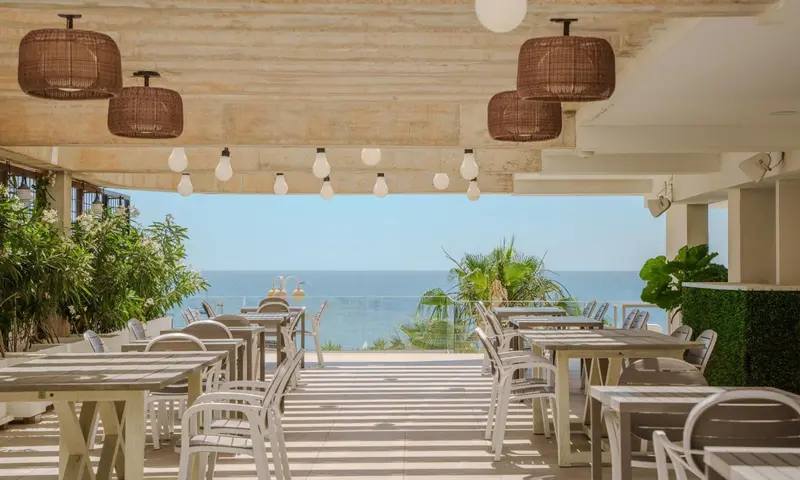 Terrasse ombragée avec tables et chaises donnant sur la mer.